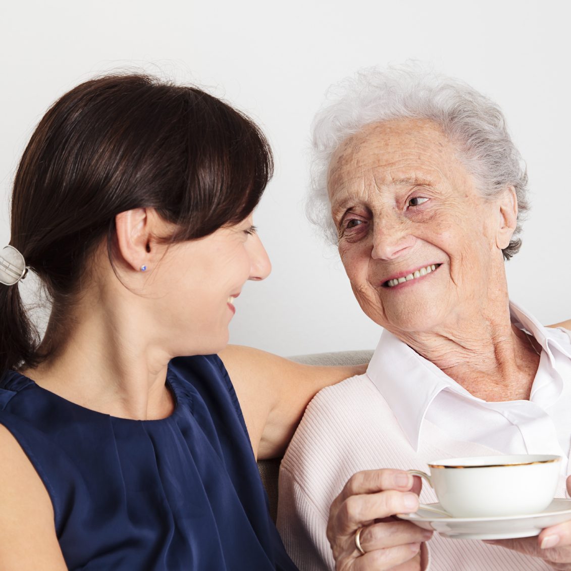 A smiling young woman and an elderly woman sharing a moment over tea.