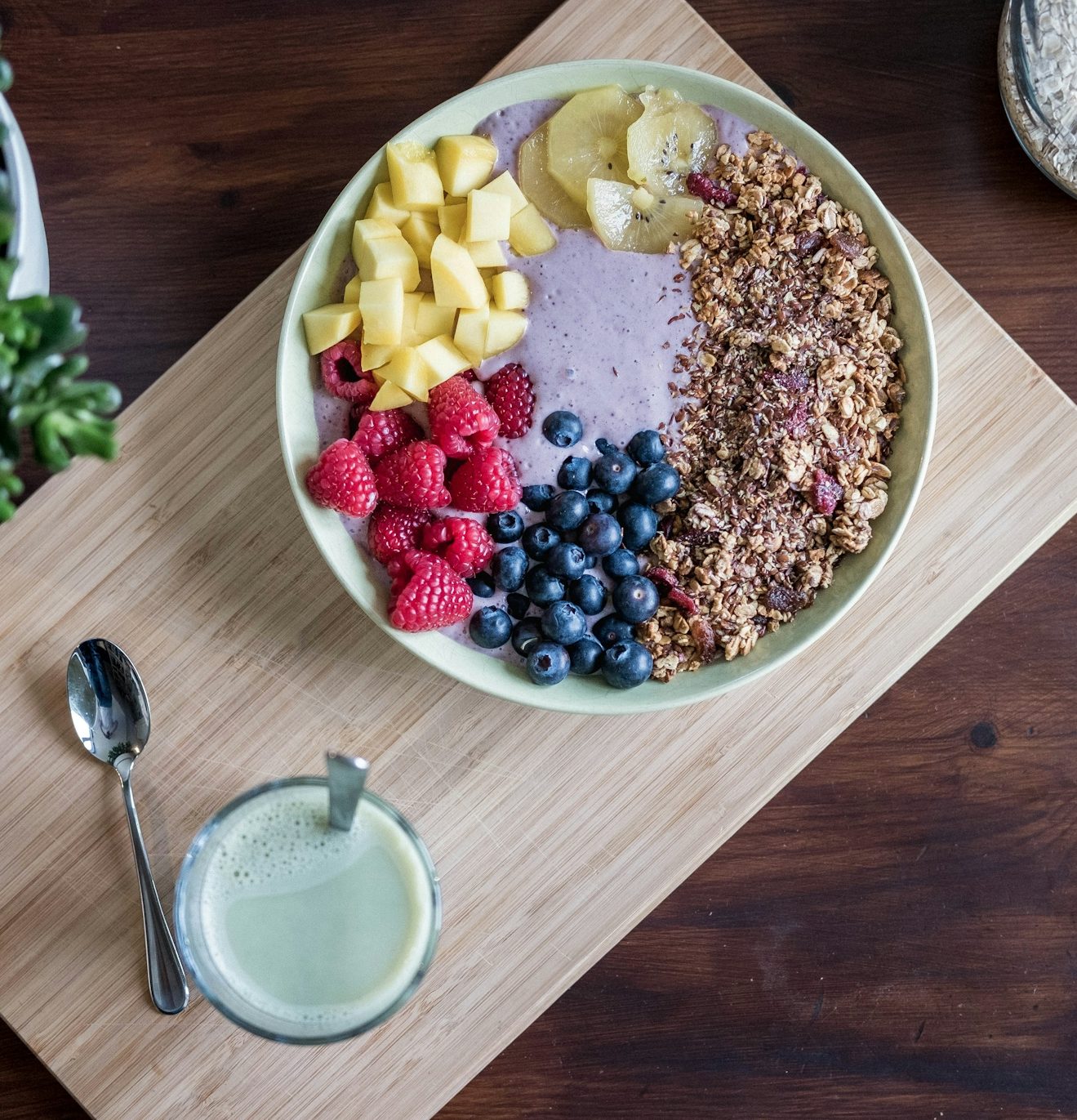 Breakfast bowl with smoothie, granola, and assorted fruits including banana and berries.