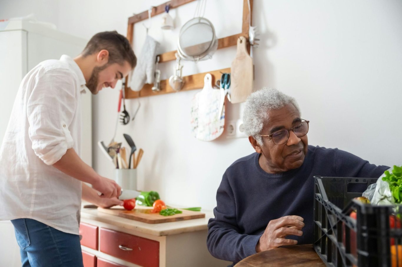 Carer cutting vegetables while man unpacks shopping