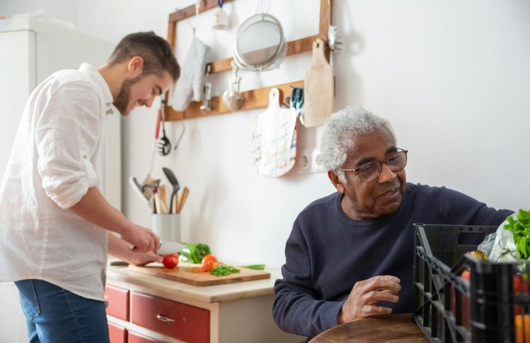 A young man chops vegetables while an elderly man organizes a basket nearby.