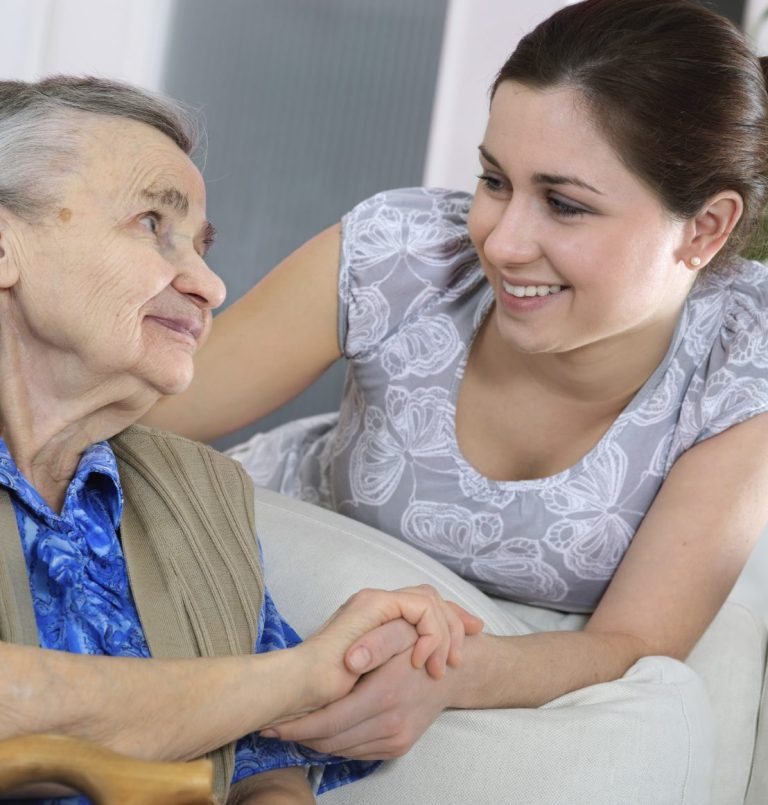 A young woman smiling while holding hands with an elderly woman in a warm conversation.